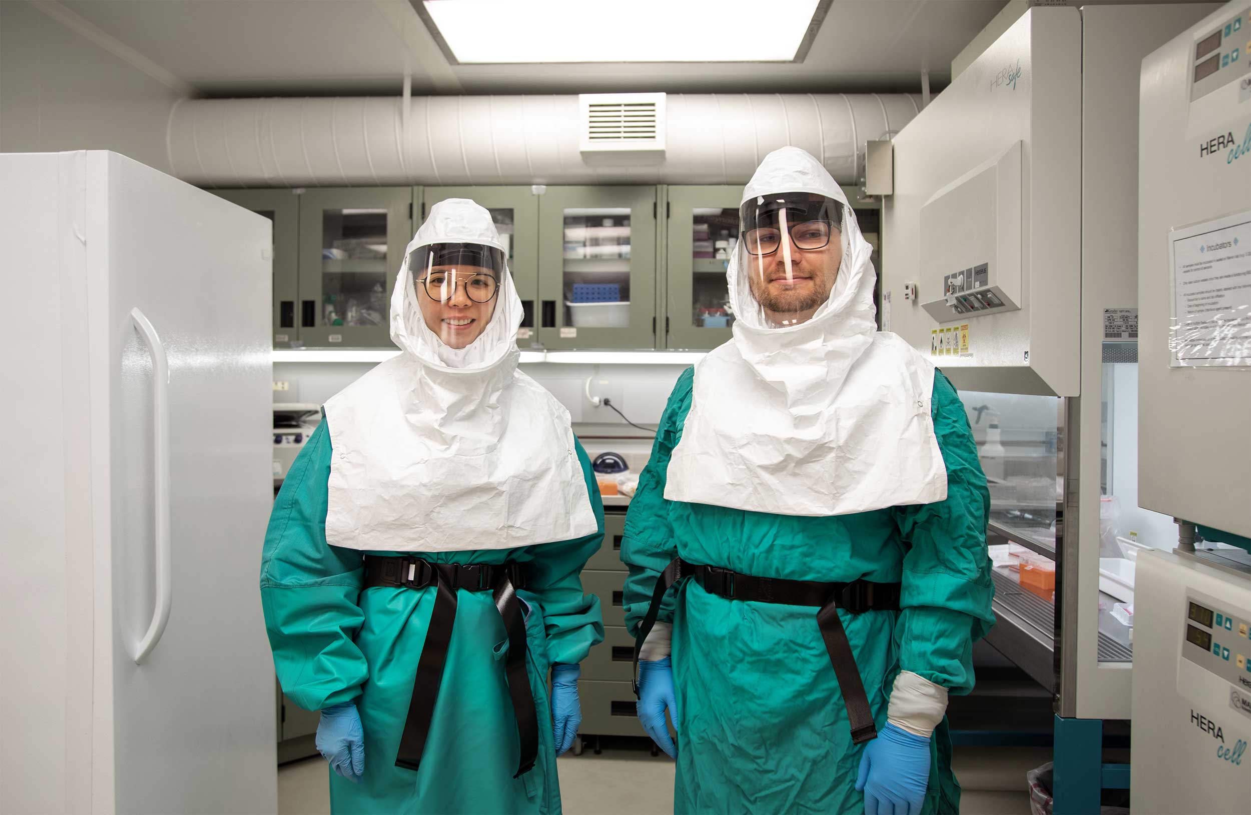 Betty Poon and Patrick Budylowski, wearing turquoise gowns, and white head gear, in the lab