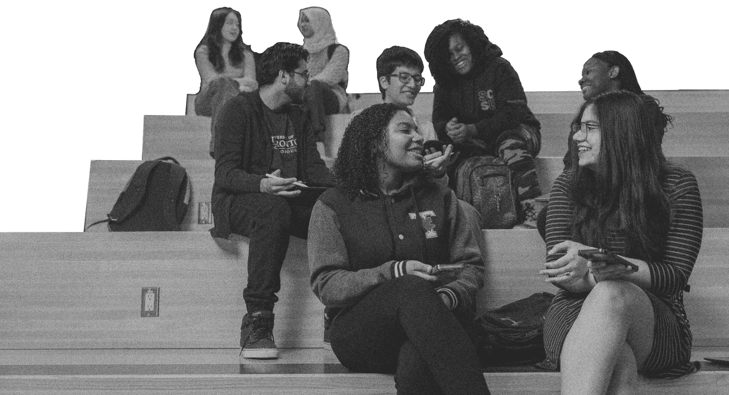 Black and white, grainy image of students in conversation with one another, sitting on bleachers in a lecture hall at UTSC