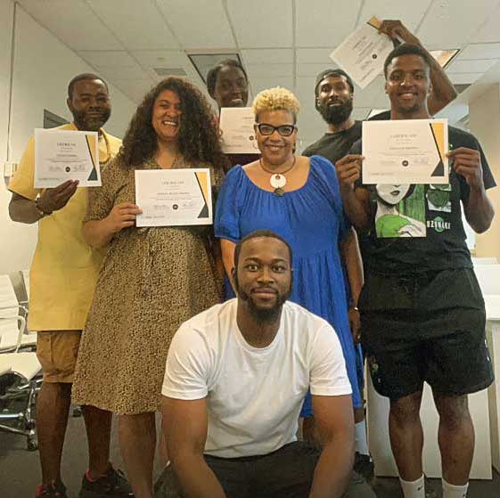 A group shot of 7 smiling people, 3 holding certificates and one sitting in the front of the group