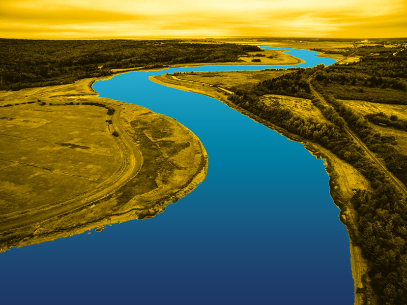 A yellow-graded image of a landscape, with a (blue-graded) river snaking through it from foreground to the horizon line.