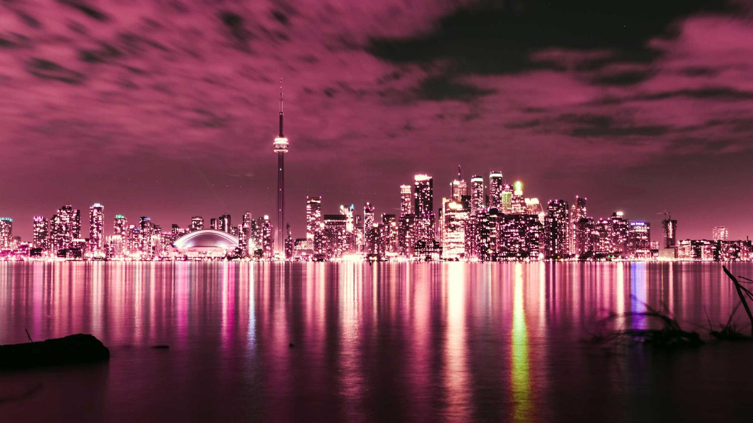 Magenta colourised night view of the city of Toronto’s skyline with lights reflecting in the lake