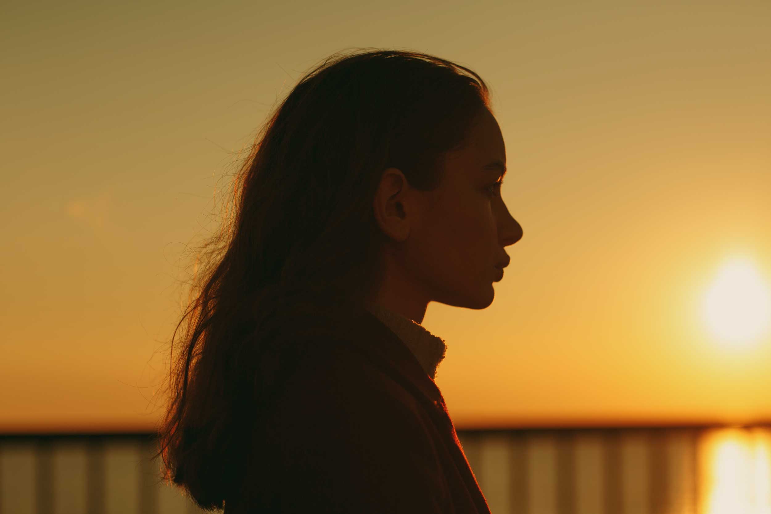 Shoulders-up, side-view, silhouette of a young woman against a yellow, sunset sky