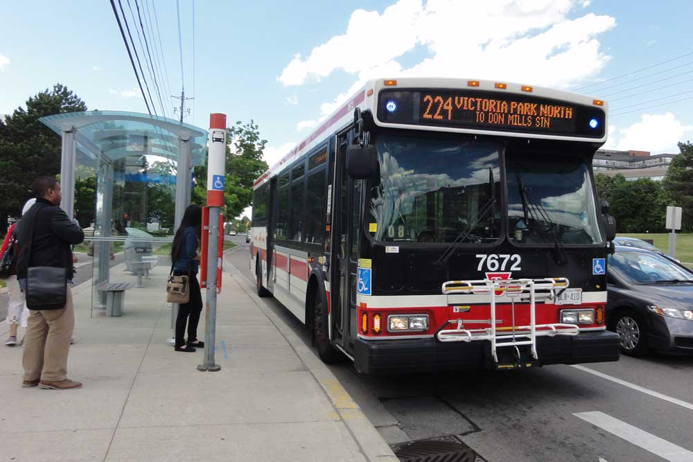 Front facing view of a TTC bus (#224) pulled over at a bus stop to pick up three passengers